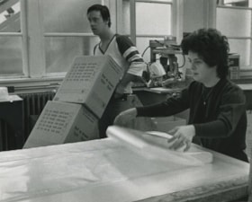 Harry Manders moves boxes while Angela Bedard rolls plastic, ca.1983 thumbnail