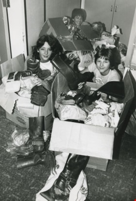 Three unidentified people covered in boxes of shoes and clothes, ca.1982 thumbnail