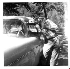 Gerald Sanders shaving using a car side mirror, [195-] thumbnail