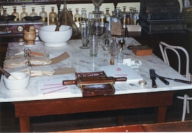 Apothecary items on marble table top inside Burnaby Village Museum Pharmacy, [198-] thumbnail
