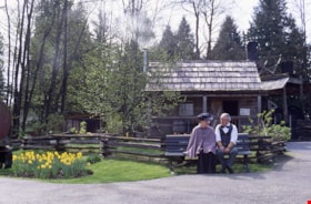 Interpreters seated on bench in front of log cabin, [1986] thumbnail