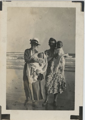 Two women holding babies on a beach, [193-] thumbnail