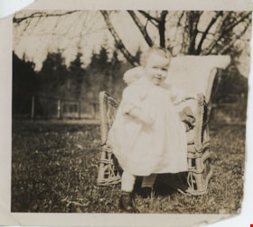Toddler standing in yard with wicker chair, [191-] thumbnail