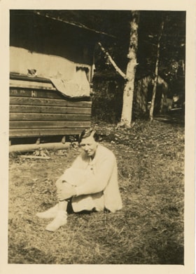 Woman seated on ground outside of cabin, [193-] thumbnail